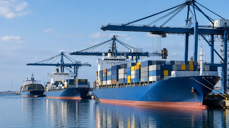 Tre store containerskibe ved kaj under høje havnekraner i en containerhavn